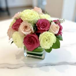 Pink and pale yellow roses arranged in a square glass vase