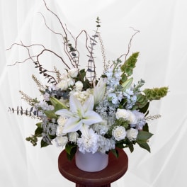White floral arrangement with lilies and roses in a pale vase
