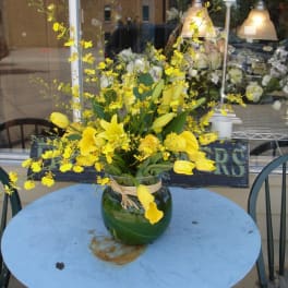 Yellow orchid and calla lily arrangement in a green glass vase