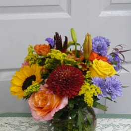 Mixed bouquet in a glass vase with roses, sunflowers, lilies, and purple blooms