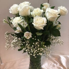 White roses and small white filler flowers in a tall glass vase