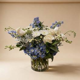 Blue and white arrangement with roses, mums, and hydrangeas in a clear glass cylinder vase