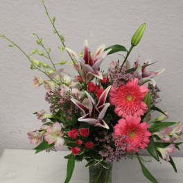 Pink gerbera daisies and lilies arranged in a glass vase