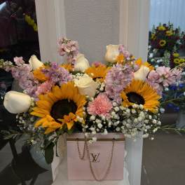 Bouquet of sunflowers, white roses, and pink flowers in a pink gift bag
