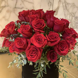Red roses arranged in a black round box with trailing greenery
