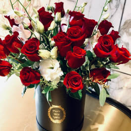 Red roses and white blooms arranged in a black hatbox