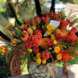 Mixed bouquet of roses and tulips in a decorative vase with pumpkins