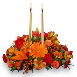 Low centerpiece of orange and red flowers with two tall gold taper candles in the center