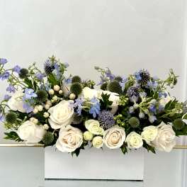 White roses and blue flowers arranged in a white box