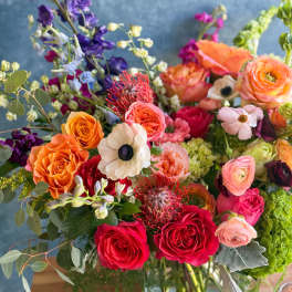 Colorful mixed bouquet of roses, ranunculus, and other blooms in a glass vase
