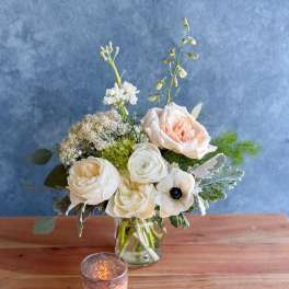 Cream and blush flowers arranged in a clear glass vase with a candle in front.
