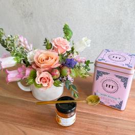 Pink and peach rose arrangement in a white mug with tea and honey gift items