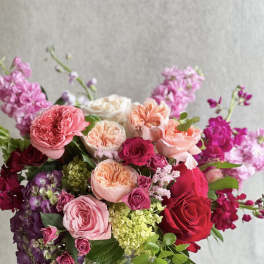 Pink and red roses arranged in a clear glass vase with purple blooms