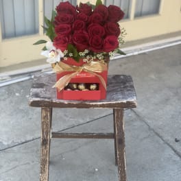 Red rose arrangement in a red gift box with chocolates and a gold ribbon