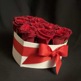 Red roses arranged in a white heart-shaped box with a red ribbon