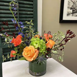 Orange and coral roses in a glass vase with blue flowers