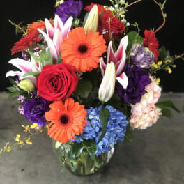 Mixed bouquet of roses, gerbera daisies, lilies, and hydrangeas in a glass vase