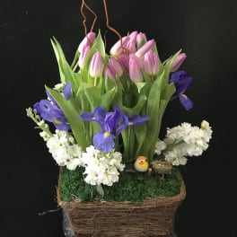 Pink tulips and purple irises in a woven basket with white flowers