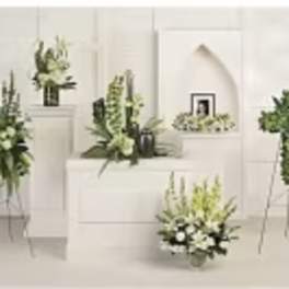 Several white and green floral arrangements on stands and pedestals in a bright room.