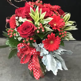 Red roses and gerbera daisies in a glass vase with a red ribbon