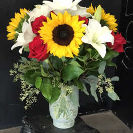 Bouquet of sunflowers, white lilies, and red roses in a textured vase