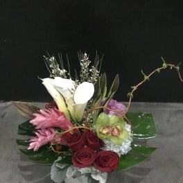 Mixed floral arrangement with white calla lilies, pink blooms, and red roses in a white vase