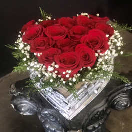 Heart-shaped bouquet of red roses with white baby's breath in a clear vase