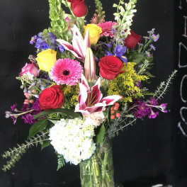 Mixed bouquet of roses, lilies, and gerbera daisies in a glass vase