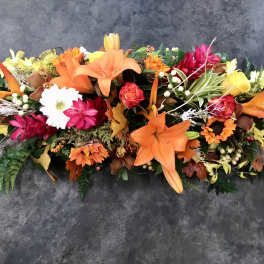 Long floral arrangement with orange lilies and mixed blooms on a dark surface