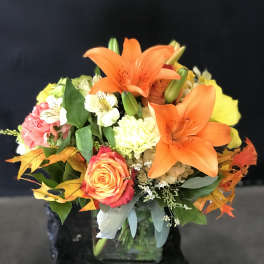 Orange lilies and roses in a glass vase with autumn leaves