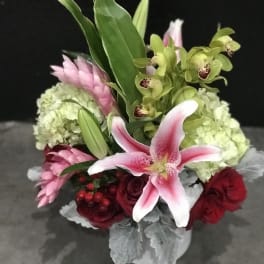 Bouquet of pink lilies, green orchids, and red roses in a white vase