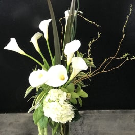 Tall arrangement of white calla lilies and hydrangea in a clear glass vase
