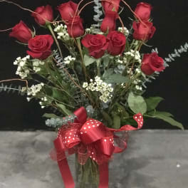 Red roses arranged in a glass vase with a red ribbon bow