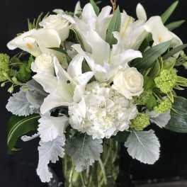 White lilies and roses arranged in a glass vase with green accents