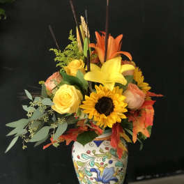 Colorful bouquet of roses, lilies, and a sunflower in a painted vase
