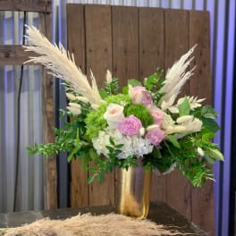 Pink and white floral arrangement in a gold vase with pampas grass