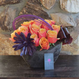 Orange and pink roses in a dark vase with purple decorative accents