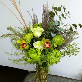 Green floral arrangement in a glass vase with orchids and hydrangeas