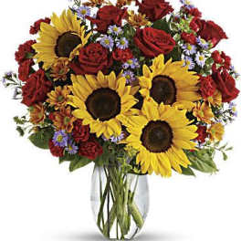 Bouquet of sunflowers, red roses, and small purple flowers in a glass vase