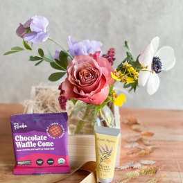 Small floral arrangement with a pink rose in a glass vase, plus chocolate and hand cream