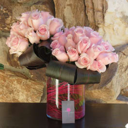 Two bouquets of pale pink roses in a glass vase with black ribbon