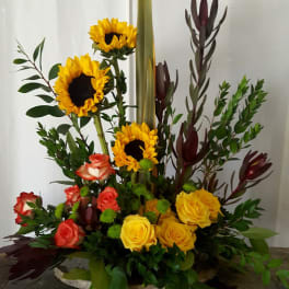 Tall floral arrangement with sunflowers and roses in yellow, coral, and red.