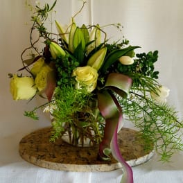 Yellow roses and lilies in a glass vase with trailing ribbon