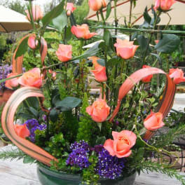 Tall arrangement of peach roses in a green bowl with ribbon loops