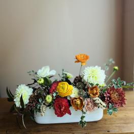Mixed flower arrangement in a white rectangular vase with orange, red, yellow, and white blooms