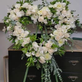 Heart-shaped white floral wreath with roses and lilies on a stand