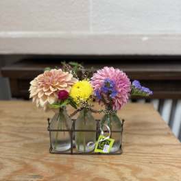 Three small glass bottles hold colorful flowers in a metal caddy.