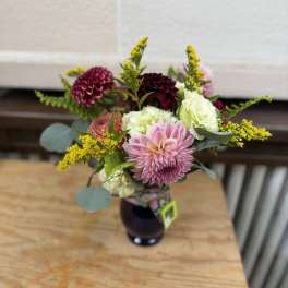Mixed bouquet with pink, white, and burgundy blooms in a dark vase