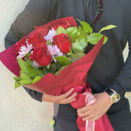 Bouquet of red roses and pale purple daisies wrapped in pink paper