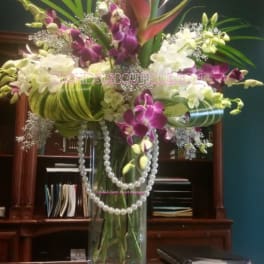 Tall orchid arrangement in a clear glass vase with pearl strands
